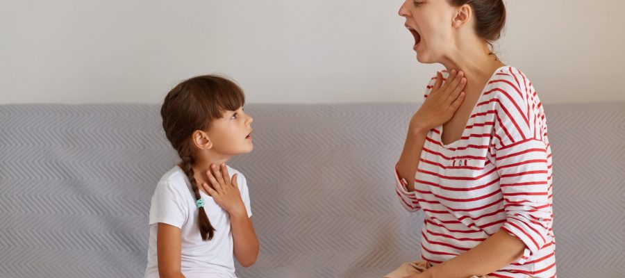 Side view portrait of speech pathologist demonstrating for little kid how to pronounce sounds right, Professional physiotherapist working on speech defects with small child girl indoors.